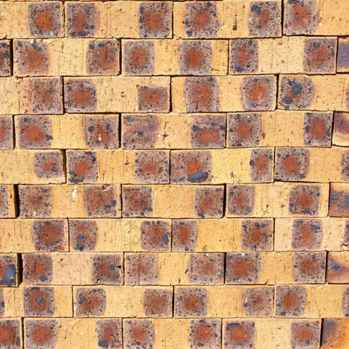 Sunrise Travertine Face Brick featuring a vibrant orange and golden clay tone with a deeply pitted, stone-like texture for exterior walls.