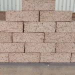 Outdoor pyramid stack of Artisanal Honey face bricks displaying heavily grooved rustic texture, warm honey-buff color, and dark iron spots.