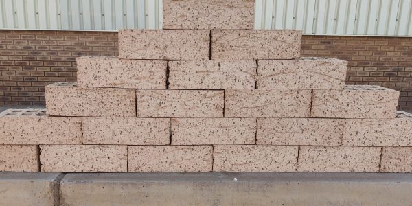 Outdoor pyramid stack of Artisanal Honey face bricks displaying heavily grooved rustic texture, warm honey-buff color, and dark iron spots.