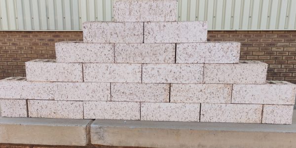 Outdoor pyramid stack of Artisanal Vanilla face bricks displaying heavily grooved rustic texture, pale cream-white color, and dark iron spots.