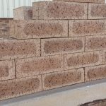 Outdoor pyramid stack of Autumn Wheat Travertine face bricks showing pitted travertine surface texture, golden-wheat and central flashed tones, and dark iron spots.