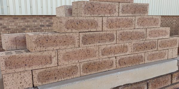 Outdoor pyramid stack of Autumn Wheat Travertine face bricks showing pitted travertine surface texture, golden-wheat and central flashed tones, and dark iron spots.
