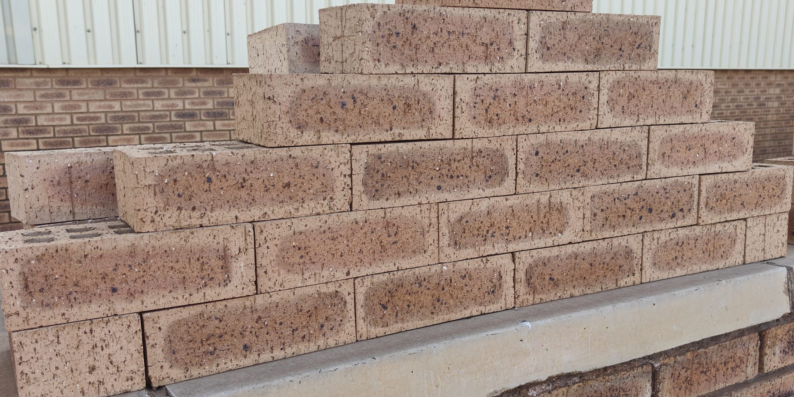 Outdoor pyramid stack of Autumn Wheat Travertine face bricks showing pitted travertine surface texture, golden-wheat and central flashed tones, and dark iron spots.