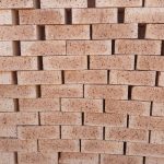 Close-up wall view of stacked Autumn Wheat Travertine face bricks showing light golden-wheat face tones, pitted travertine texture, and dark iron spots.