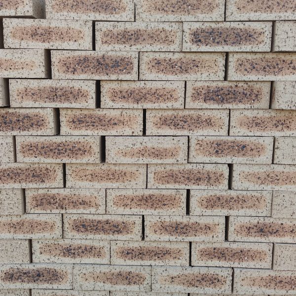 Front-on view of stacked Blue Barley Travertine face bricks showing light barley-cream clay body with dark flashed central spots and pitted travertine texture.