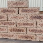 Outdoor pyramid stack of Blue Barley Travertine face bricks displaying light barley-cream face tones, dark flashed central cores, pitted travertine texture, and iron spots.