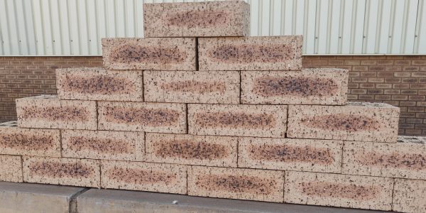 Outdoor pyramid stack of Blue Barley Travertine face bricks displaying light barley-cream face tones, dark flashed central cores, pitted travertine texture, and iron spots.