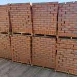 Outdoor yard view of multiple timber pallets stacked with Country Classic Satin face bricks showing rich terracotta body, blue-grey central kiln flashing, and smooth satin texture.