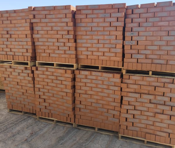 Outdoor yard view of multiple timber pallets stacked with Country Classic Satin face bricks showing rich terracotta body, blue-grey central kiln flashing, and smooth satin texture.