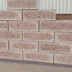 Outdoor pyramid stack of Golden Wheat Travertine face bricks displaying pitted travertine texture, warm golden-wheat body, dark flashed centers, and iron speckling.