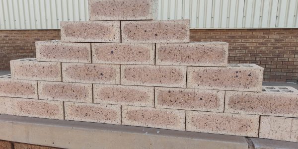 Outdoor pyramid stack of Golden Wheat Travertine face bricks displaying pitted travertine texture, warm golden-wheat body, dark flashed centers, and iron speckling.