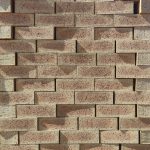 Front-on view of stacked Golden Wheat Travertine face bricks showing warm golden-wheat clay body, pitted travertine surface texture, soft central flashed spots, and iron speckling under sunlight.