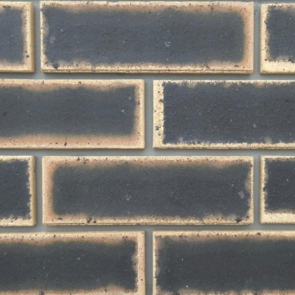 Close-up of Granite Satin Face Bricks laid in a wall section with grey mortar, showing dark center flashes with light tan borders.