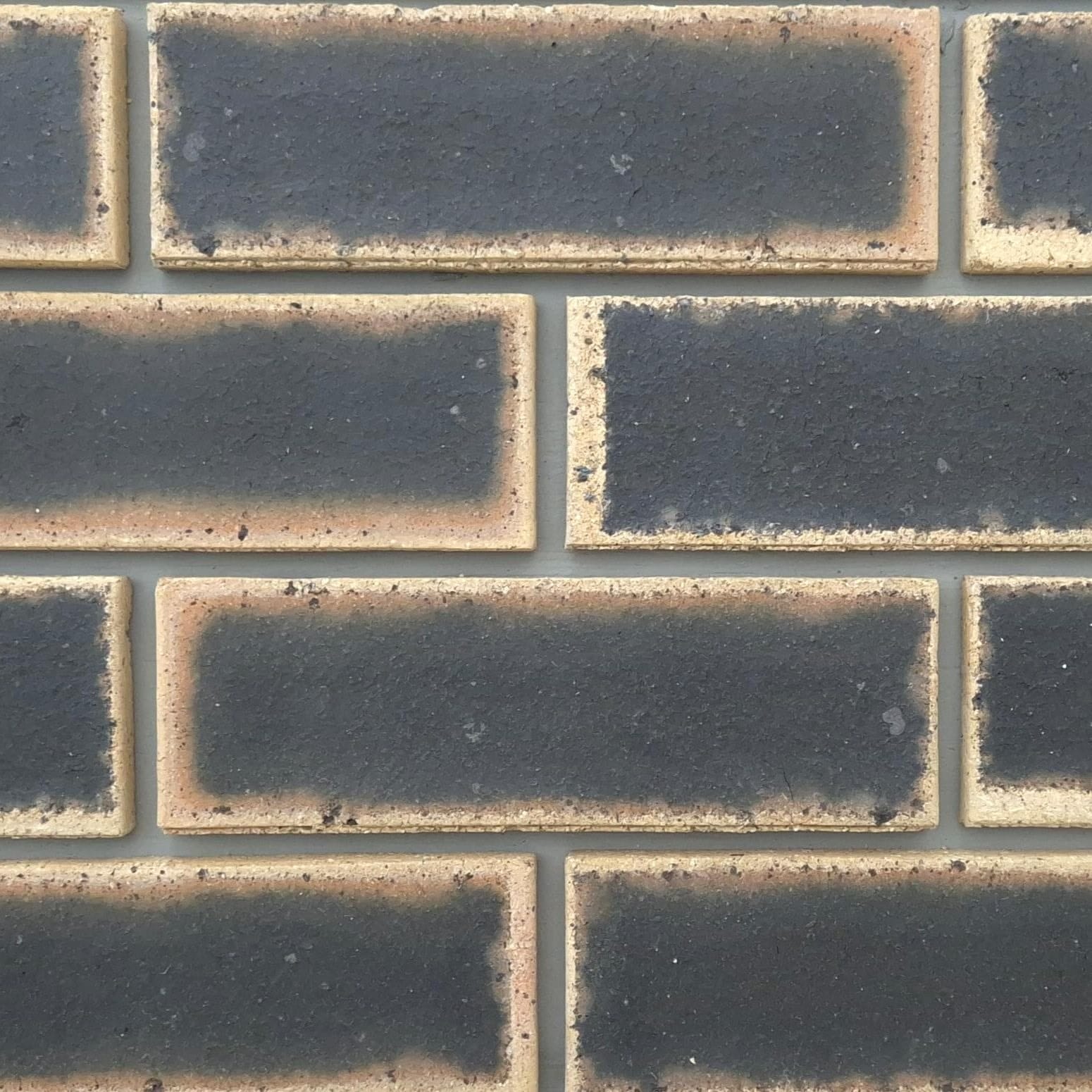 Close-up of Granite Satin Face Bricks laid in a wall section with grey mortar, showing dark center flashes with light tan borders.
