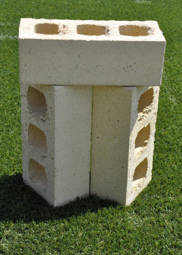 Three Ivory Satin clay face bricks stacked outdoors on grass showing internal core hole perforations and smooth cream finish.