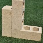 Three Ivory Travertine clay face bricks displayed on grass showing rustic travertine texture, light beige color, and core perforations.