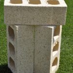Three Ivory Travertine face bricks stacked upright outdoors on grass showing internal core hole perforations and textured travertine surface finish.