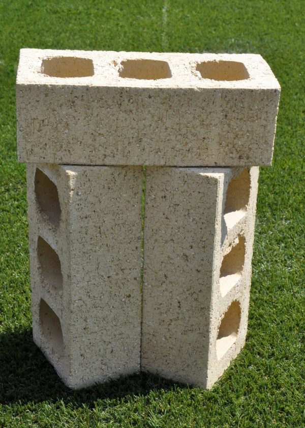 Three Ivory Travertine face bricks stacked upright outdoors on grass showing internal core hole perforations and textured travertine surface finish.
