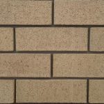 Close-up of Ivory Travertine face bricks laid in a wall panel with grey mortar joints showing rustic pitted travertine texture and uniform cream color.