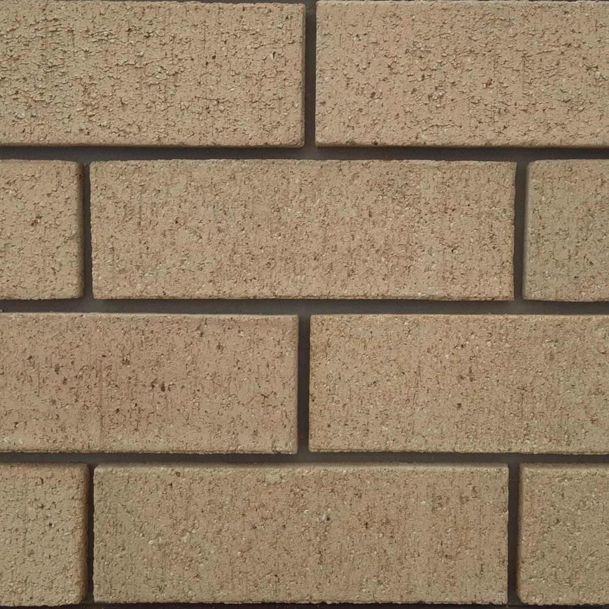Close-up of Ivory Travertine face bricks laid in a wall panel with grey mortar joints showing rustic pitted travertine texture and uniform cream color.