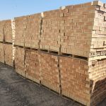 Outdoor yard view of stacked timber pallets containing Letaba Satin face bricks showing warm peach-buff tones, central heat-flashed hearts, and smooth satin finish.