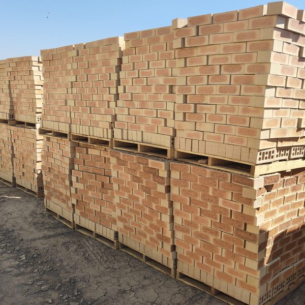 Outdoor yard view of stacked timber pallets containing Letaba Satin face bricks showing warm peach-buff tones, central heat-flashed hearts, and smooth satin finish.