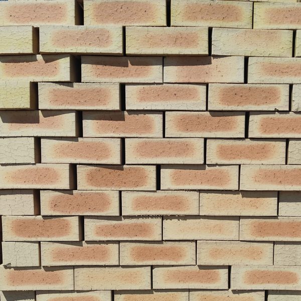 Front-on view of stacked Letaba Satin variation face bricks showing pale cream-yellow margins, smooth satin finish, and distinct soft peach-apricot flashed central cores.