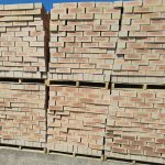 Outdoor yard view of multiple wooden pallets stacked two-high with Letaba Satin face bricks showing pale cream-buff body, light peach-apricot flashed centers, and smooth satin finish.