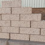 Outdoor pyramid stack of Maize Travertine face bricks displaying light cream-maize body tones, heavy iron speckling, and pitted travertine finish.