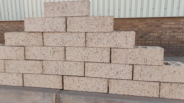 Outdoor pyramid stack of Maize Travertine face bricks displaying light cream-maize body tones, heavy iron speckling, and pitted travertine finish.
