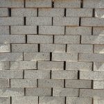 Front-on view of stacked Maize Travertine face bricks showing light cream-maize clay body, pitted travertine texture, and fine manganese iron speckling under sunlight.