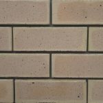 Close-up of Marble Satin face bricks laid in a wall section showing subtle pink-tan hues, smooth satin finish, and dark iron spot speckling.