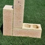 Three Marble Travertine clay face bricks displayed outdoors on grass showing pitted travertine surface texture, light peach-tan tones, and core holes.