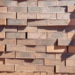 Front-on view of stacked Moroccan Red Travertine Dark face bricks showing pitted travertine surface texture, warm terracotta clay body, dark charcoal heat flashing, and fine iron speckling.