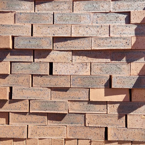 Front-on view of stacked Moroccan Red Travertine Dark face bricks showing pitted travertine surface texture, warm terracotta clay body, dark charcoal heat flashing, and fine iron speckling.
