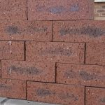 Outdoor pyramid stack of Namib Red Travertine face bricks displaying pitted travertine texture, rich deep red clay body, and dark charcoal heat-flashed centers.