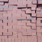 Front-on view of stacked Namib Red Travertine face bricks showing pitted travertine texture, rich deep red clay body, and dark charcoal heat-flashed central markings under direct sunlight.