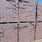 Outdoor yard view of multiple wooden pallets stacked two-high with Namib Red Travertine face bricks showing deep red clay body, dark blue-charcoal heat-flashed centers, and pitted travertine finish.