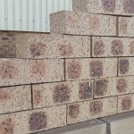 Outdoor pyramid stack of Nebraska Travertine face bricks displaying pitted travertine texture, pale buff-cream body, and distinct dark charcoal-brown heat-flashed centers with heavy iron speckling.
