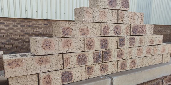 Outdoor pyramid stack of Nebraska Travertine face bricks displaying pitted travertine texture, pale buff-cream body, and distinct dark charcoal-brown heat-flashed centers with heavy iron speckling.