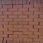 Front-on view of stacked Redwood Travertine Light face bricks showing pitted travertine surface texture, warm terracotta-red clay body, and distinct light orange-apricot flashed center cores.