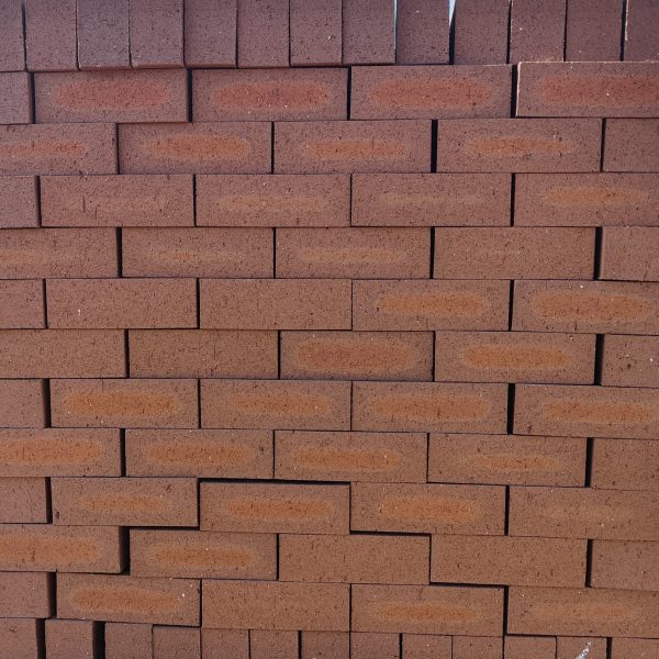 Front-on view of stacked Redwood Travertine Light face bricks showing pitted travertine surface texture, warm terracotta-red clay body, and distinct light orange-apricot flashed center cores.
