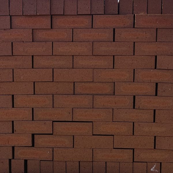 Front-on view of stacked Redwood Travertine Light face bricks showing pitted travertine surface texture, warm terracotta-red clay body, and distinct light orange-apricot flashed center cores.