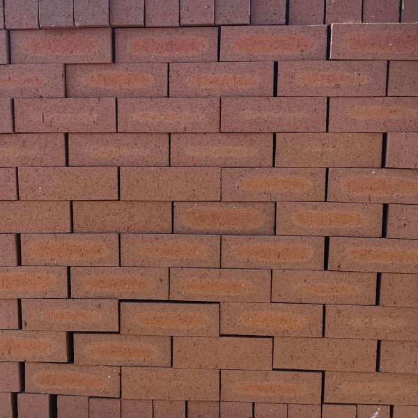 Front-on view of stacked Redwood Travertine Light face bricks showing pitted travertine surface texture, warm terracotta-red clay body, and distinct light orange-apricot flashed center cores.