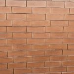Front-on view of stacked Ruby Light Satin face bricks showing smooth satin surface texture, warm terracotta-peach clay body, and subtle iron speckling under bright sunlight.