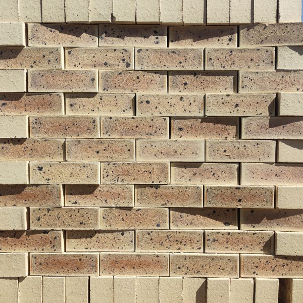 Front-on view of stacked Sapphire Satin Light face bricks showing smooth satin finish, light cream-buff clay body, subtle golden-brown heat flashing, and distinct dark iron spots.