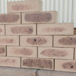 Outdoor pyramid stack display of Savanna Satin face bricks showing smooth satin texture, pale golden-wheat clay body, dark charcoal heat-flashed centers, and iron speckling.
