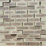 Front-on view of stacked Savanna Satin face bricks showing smooth satin finish, light wheat-cream clay body, dark grey-purple heat-flashed centers, and iron speckling under bright daylight.