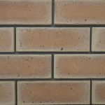Close-up of Sunrise Satin face bricks laid in a wall panel with dark mortar joints showing warm golden-orange tones, smooth satin finish, and iron spots.