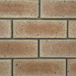 Close-up of Sunrise Travertine face bricks laid in a wall panel with grey mortar joints showing pitted travertine texture, warm apricot-golden hues, and iron spots.